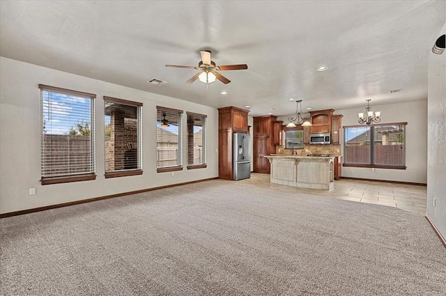 unfurnished living room featuring ceiling fan with notable chandelier, light carpet, and a wealth of natural light