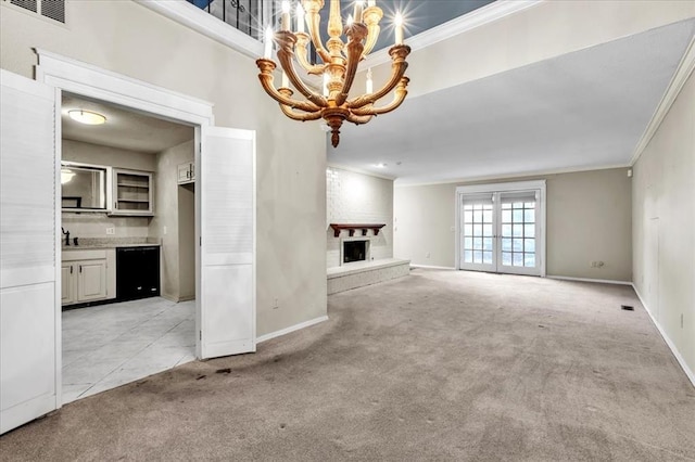 unfurnished living room with sink, a large fireplace, an inviting chandelier, crown molding, and light colored carpet