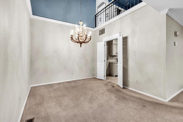 carpeted empty room featuring a high ceiling, an inviting chandelier, and crown molding