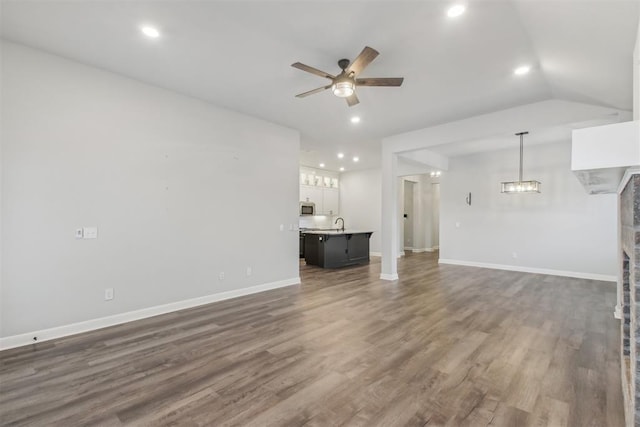 unfurnished living room featuring vaulted ceiling, dark hardwood / wood-style floors, and ceiling fan with notable chandelier