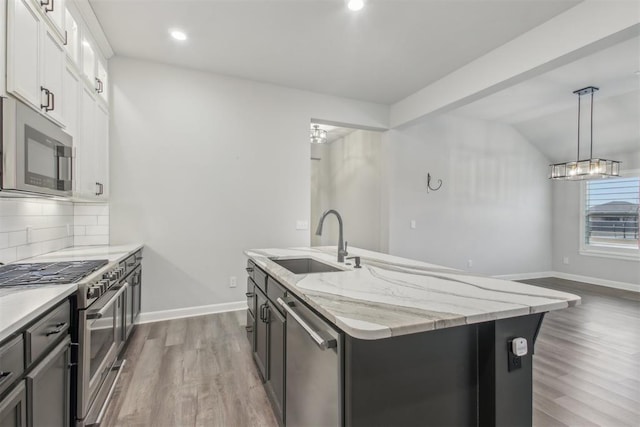 kitchen with sink, white cabinetry, a center island with sink, stainless steel appliances, and light stone countertops