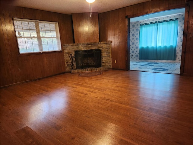 unfurnished living room with wood-type flooring, a textured ceiling, a brick fireplace, and wood walls