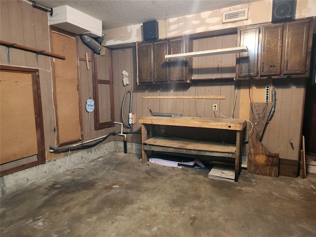 basement with a textured ceiling, a workshop area, and wood walls