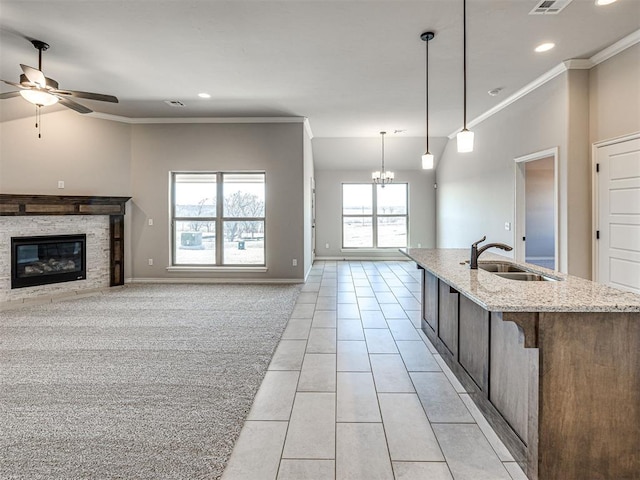 kitchen featuring light carpet, light stone counters, ceiling fan with notable chandelier, sink, and pendant lighting