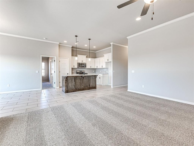 kitchen featuring pendant lighting, a center island with sink, white cabinets, crown molding, and ceiling fan