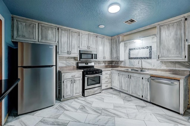 kitchen with decorative backsplash, appliances with stainless steel finishes, a textured ceiling, and sink