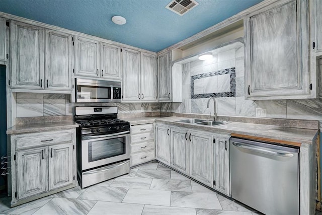 kitchen featuring a textured ceiling, decorative backsplash, sink, and appliances with stainless steel finishes