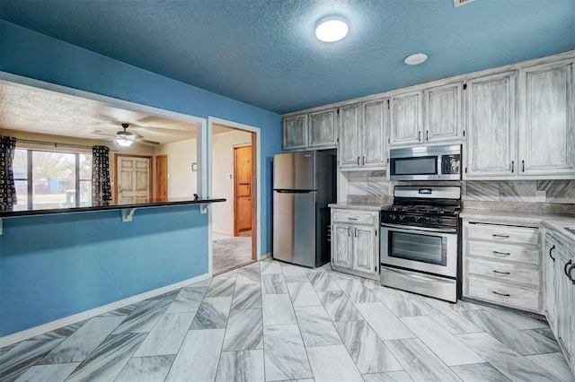 kitchen with appliances with stainless steel finishes, a textured ceiling, ceiling fan, and backsplash