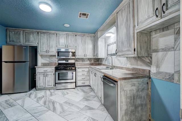 kitchen featuring a textured ceiling, backsplash, sink, and stainless steel appliances