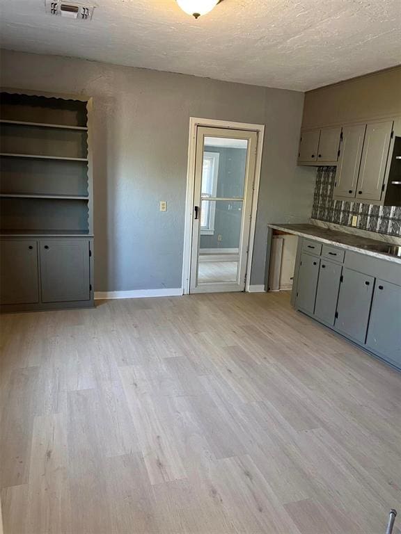 kitchen featuring gray cabinetry, sink, a textured ceiling, tasteful backsplash, and light hardwood / wood-style floors