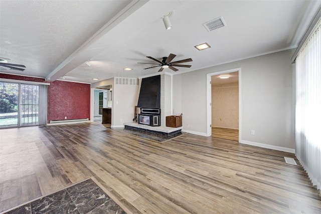 unfurnished living room featuring a wood stove, a baseboard heating unit, hardwood / wood-style flooring, ceiling fan, and a textured ceiling