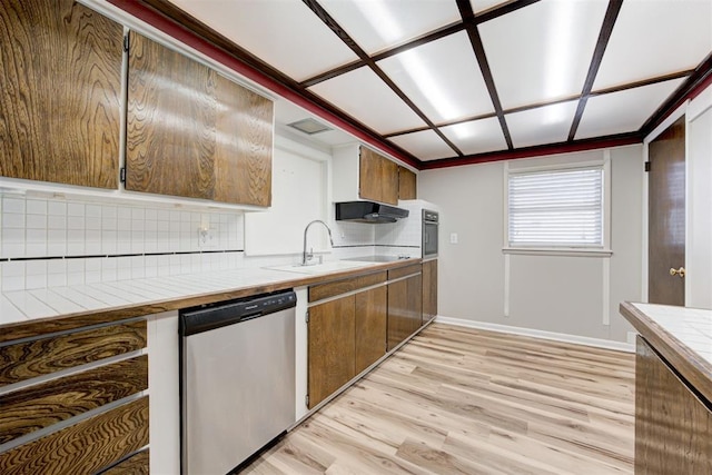 kitchen featuring tile countertops, backsplash, sink, stainless steel dishwasher, and light hardwood / wood-style floors