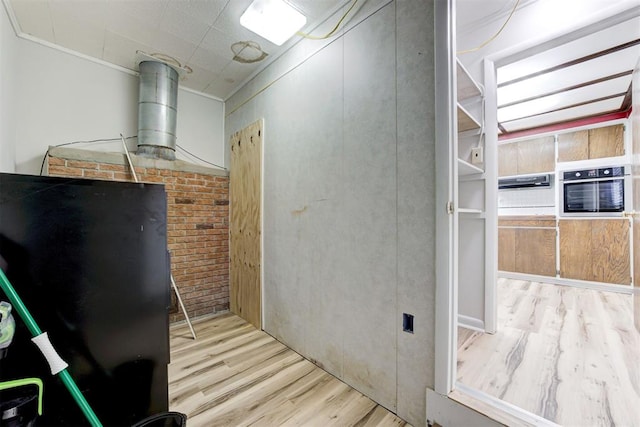 interior space with brick wall and light hardwood / wood-style flooring