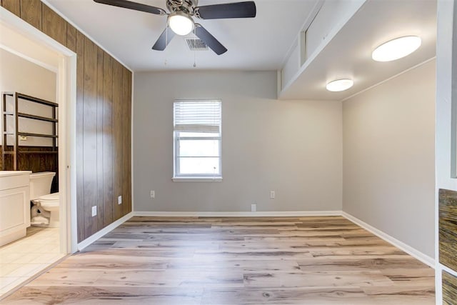 spare room featuring wood walls, ceiling fan, and light wood-type flooring