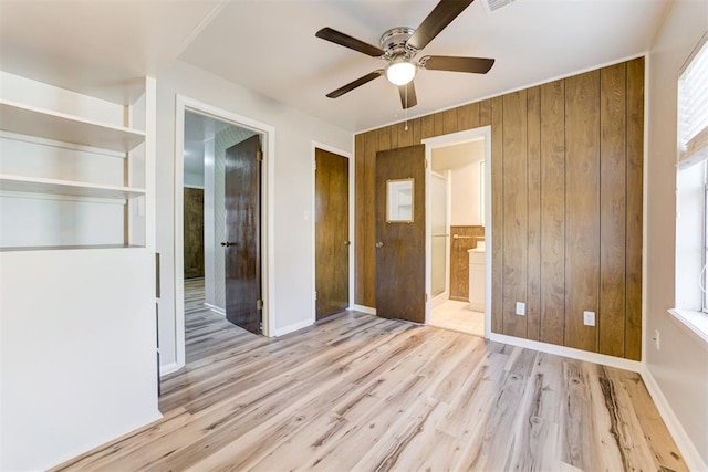 unfurnished bedroom featuring connected bathroom, light hardwood / wood-style floors, ceiling fan, and wooden walls