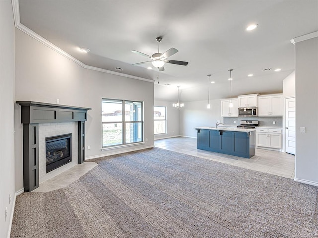 kitchen with ceiling fan with notable chandelier, stainless steel appliances, a kitchen island with sink, crown molding, and white cabinetry