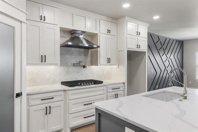 kitchen with light stone counters, black gas stovetop, wall chimney exhaust hood, sink, and white cabinets