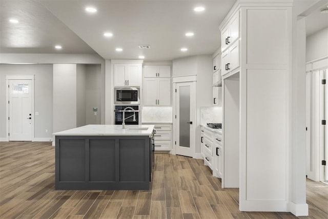 kitchen with a center island with sink, white cabinets, stainless steel appliances, and wood-type flooring