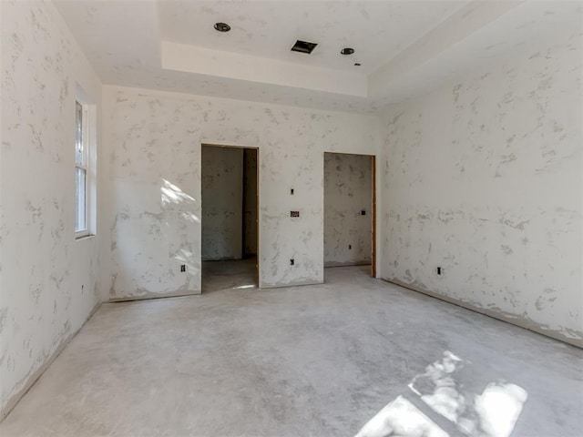 unfurnished bedroom with a tray ceiling and unfinished concrete flooring