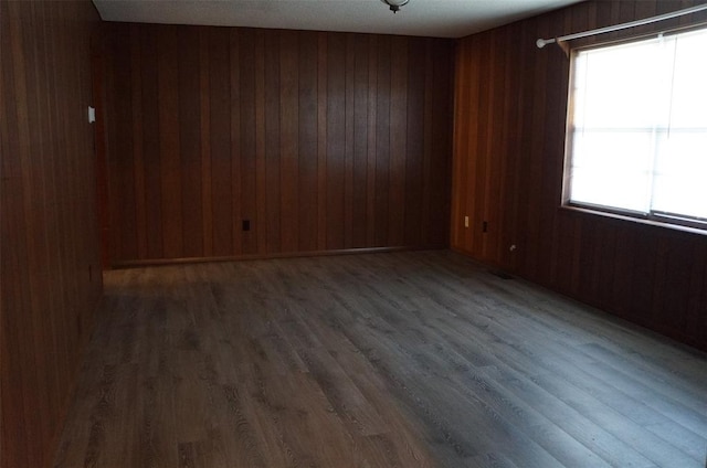 spare room featuring dark hardwood / wood-style flooring, wooden walls, and plenty of natural light