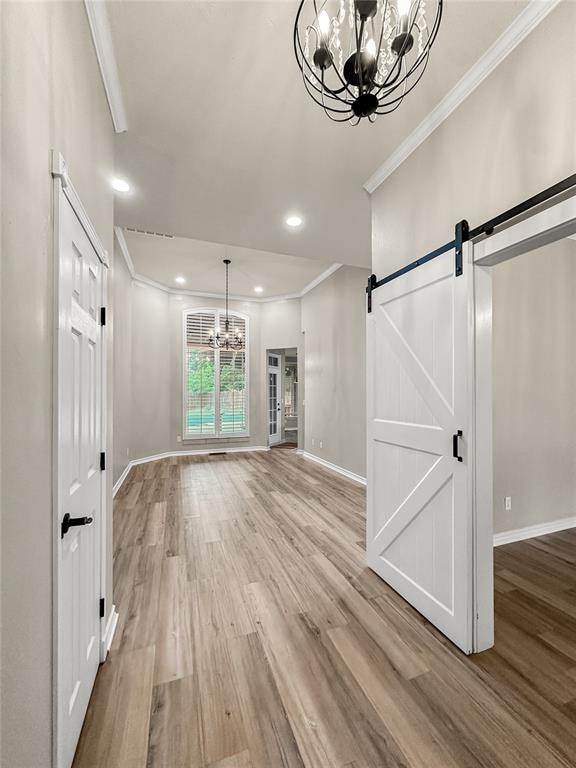 unfurnished living room featuring a barn door, crown molding, hardwood / wood-style floors, and a notable chandelier