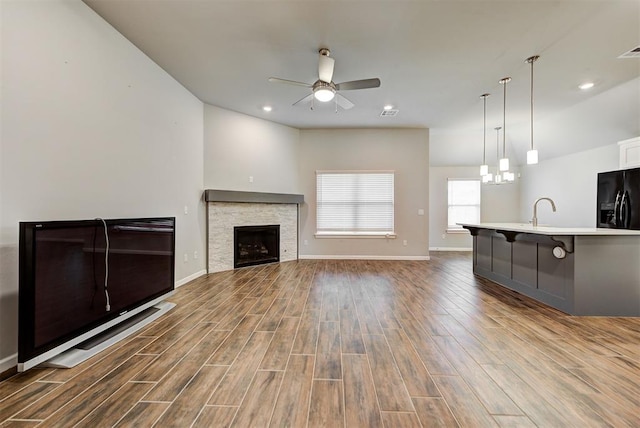 unfurnished living room with hardwood / wood-style flooring, ceiling fan, a stone fireplace, and sink