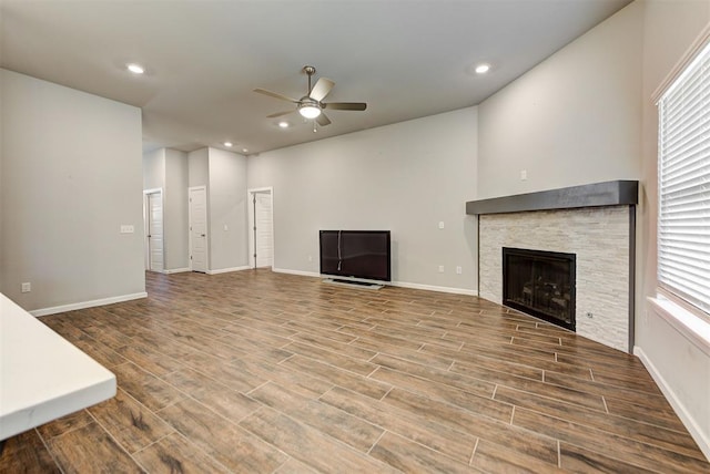 unfurnished living room with ceiling fan, a healthy amount of sunlight, a stone fireplace, and wood-type flooring