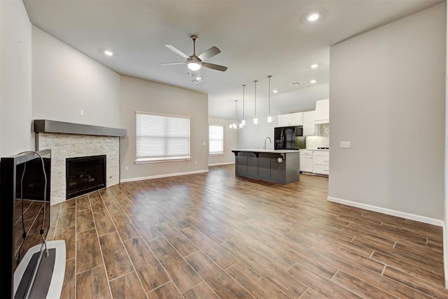 unfurnished living room with a fireplace, sink, dark wood-type flooring, and ceiling fan with notable chandelier