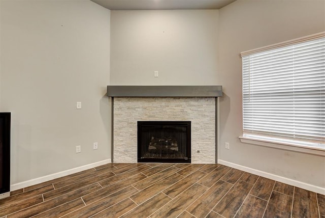 unfurnished living room featuring a stone fireplace and dark wood-type flooring