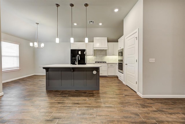 kitchen with dark wood-type flooring, stainless steel appliances, an island with sink, decorative light fixtures, and white cabinets