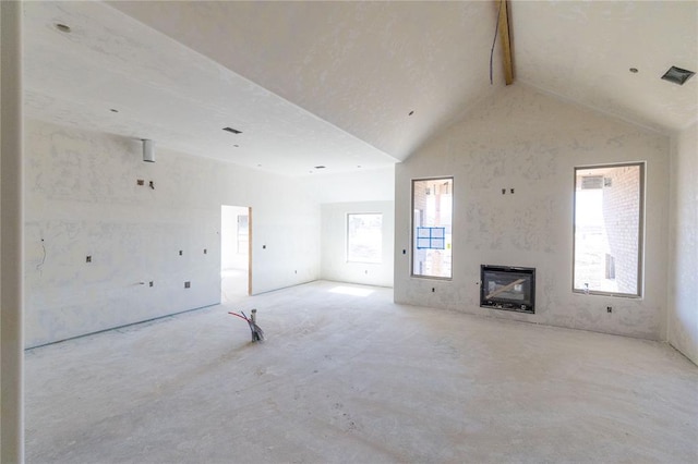 unfurnished living room featuring vaulted ceiling with beams, visible vents, a wealth of natural light, and a glass covered fireplace