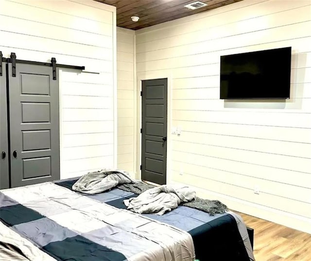 bedroom with a barn door, wood walls, wood ceiling, and hardwood / wood-style flooring