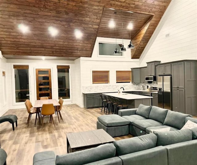 living room with light hardwood / wood-style floors, wood ceiling, sink, and high vaulted ceiling