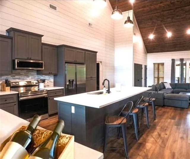 kitchen with dark hardwood / wood-style flooring, stainless steel appliances, a kitchen island with sink, high vaulted ceiling, and a breakfast bar area