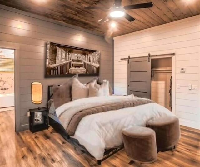 bedroom with a barn door, ceiling fan, and wood-type flooring