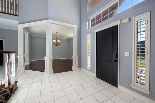 tiled entryway featuring decorative columns, ornamental molding, a towering ceiling, and a chandelier