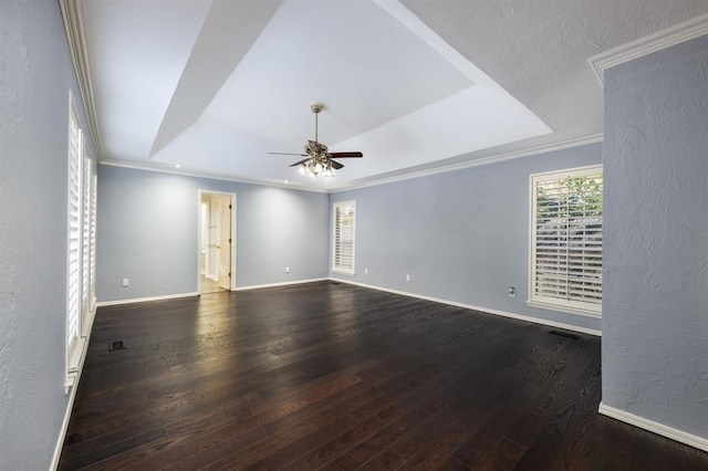 empty room featuring a raised ceiling, crown molding, ceiling fan, and dark wood-type flooring