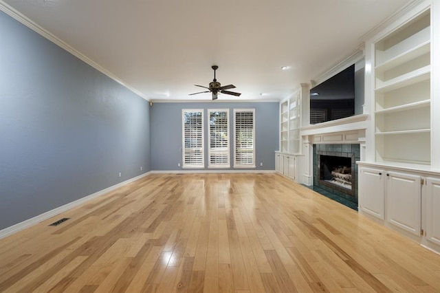 unfurnished living room featuring light wood-type flooring, built in shelves, ceiling fan, crown molding, and a fireplace