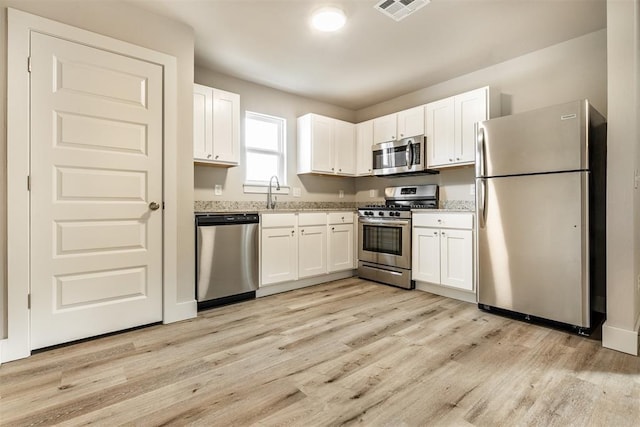 kitchen with light wood-type flooring, white cabinetry, sink, and appliances with stainless steel finishes