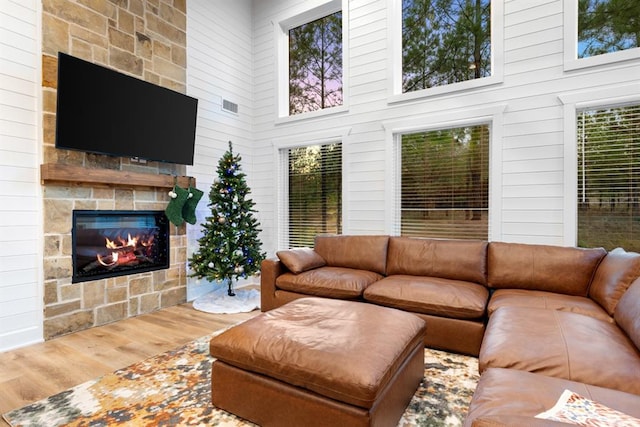 living room with a stone fireplace, a towering ceiling, and wood-type flooring