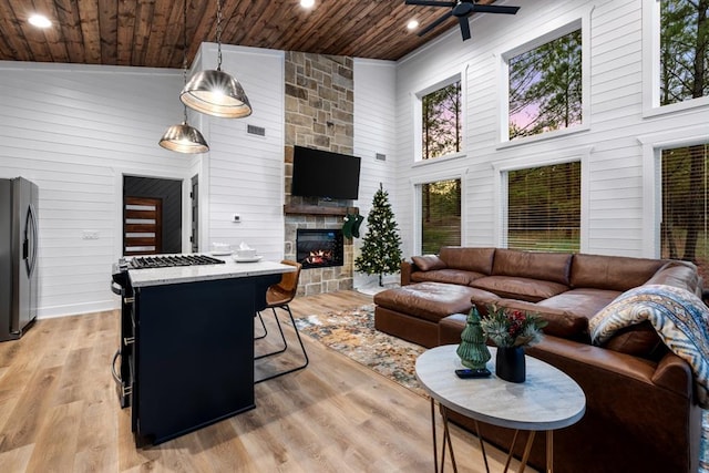 living room featuring ceiling fan, wooden ceiling, a stone fireplace, light hardwood / wood-style flooring, and high vaulted ceiling