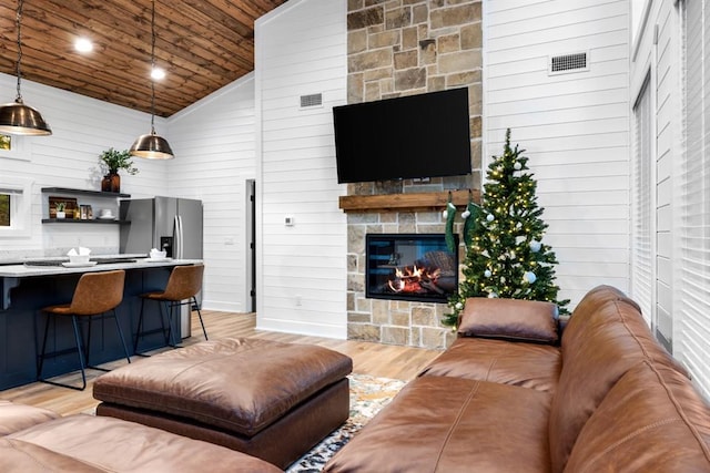 living room featuring a stone fireplace, wood walls, high vaulted ceiling, and light hardwood / wood-style floors