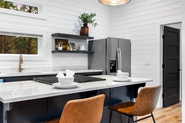 kitchen featuring stainless steel fridge with ice dispenser, a wealth of natural light, a breakfast bar, and wood walls