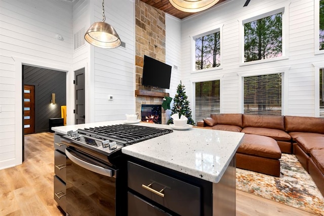 kitchen with a high ceiling, gas range, pendant lighting, and light hardwood / wood-style floors