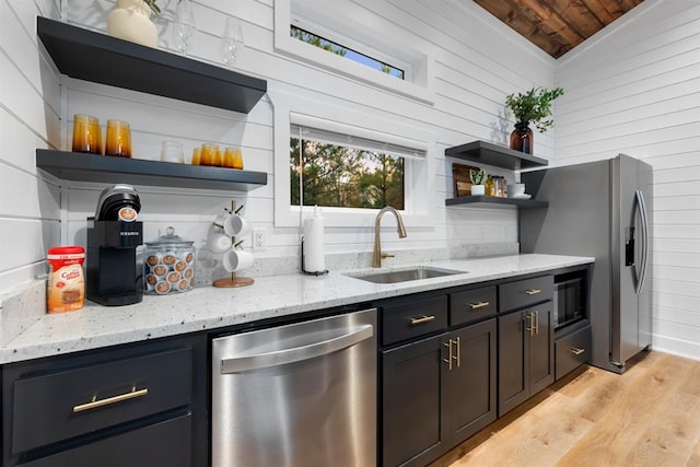 kitchen featuring light stone countertops, wooden walls, vaulted ceiling, and appliances with stainless steel finishes