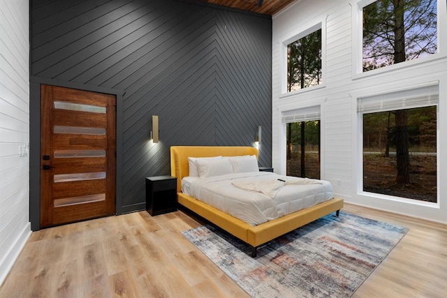 bedroom with wooden walls, light hardwood / wood-style flooring, and a towering ceiling