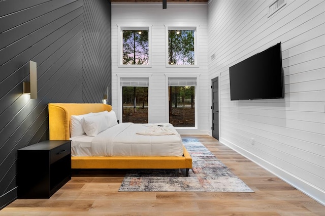 bedroom featuring a towering ceiling, light hardwood / wood-style floors, and wood walls