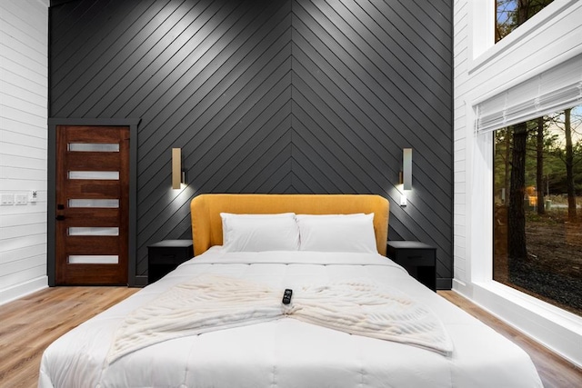 bedroom featuring wood walls, a towering ceiling, and light hardwood / wood-style floors