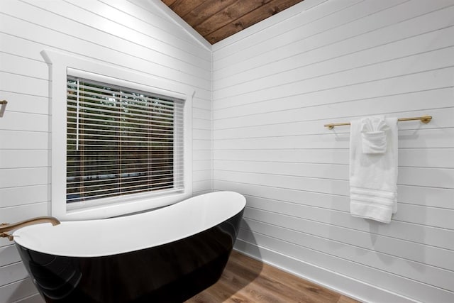 bathroom with wooden ceiling, vaulted ceiling, wooden walls, a bathtub, and hardwood / wood-style flooring