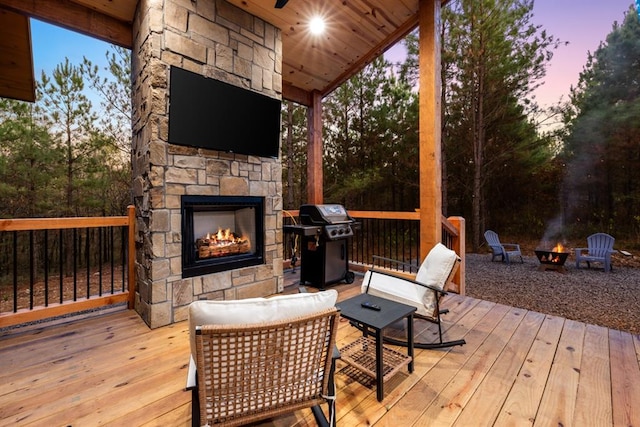 wooden deck featuring an outdoor stone fireplace and a grill